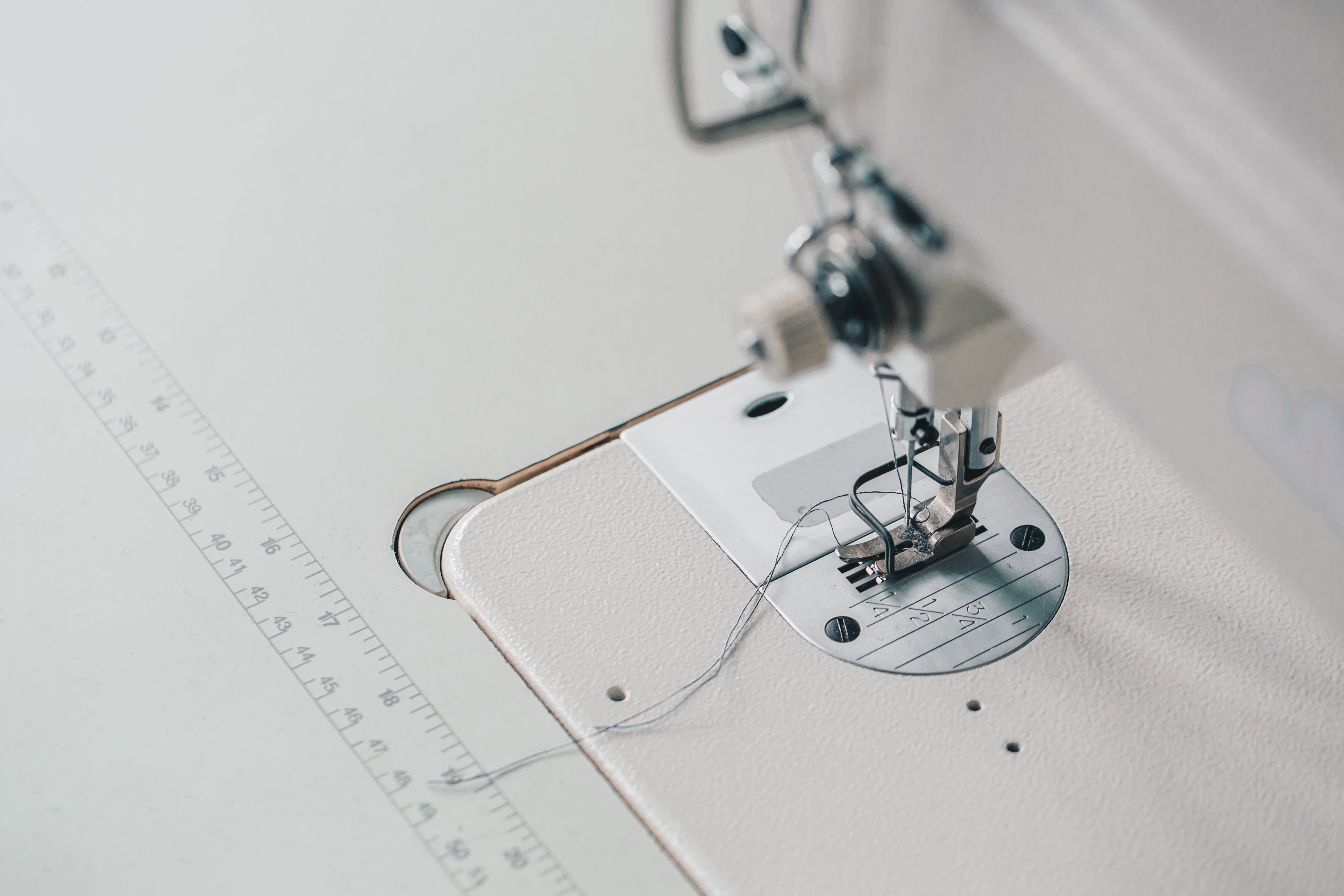 Vue en angle d'une machine à coudre avec aiguille et fil, sur une table avec règle de mesure intégrée.